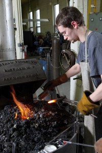 Michael Knofczynski inserts a blacksmithing tool into the hot fire.