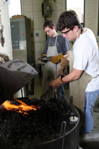 Logan Janssen, right, inserts a blacksmithing tool into the hot fire as Michael Knofczynski holds a tool for his turn at the forge.