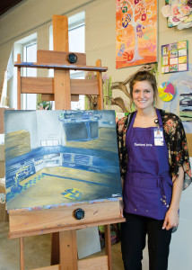 Stuart stands next to her depiction of an empty Frost Arena. Aâ€ˆmember of the womenâ€™s basketball team, Stuart chose to paint Frost Arena when challenged to paint a place filled with emotion.