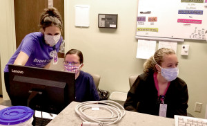 Nurses work at a computer wearing homemade cloth masks.