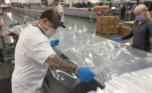 A man and woman cut a sheet of plastic.