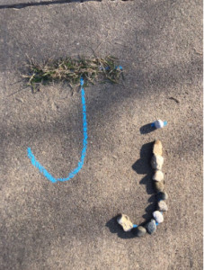 The letter 'J' written on the sidewalk in chalk and rocks.