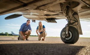 A man and woman examine the underside of an airplane.