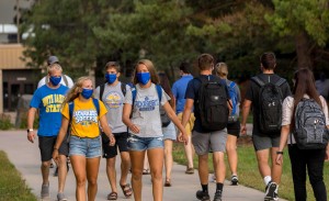 A group of students walk on campus wearing protective face coverings.