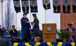 A graduate walks across the stage and fist bumps the university president as he accepts his diploma.