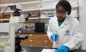 A woman wearing a lab coat and safety goggles works in a lab on an experiment.