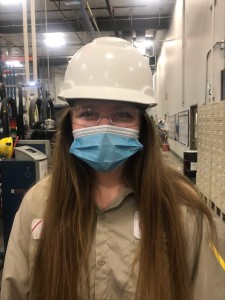 A woman wears a hard hat and a mask.