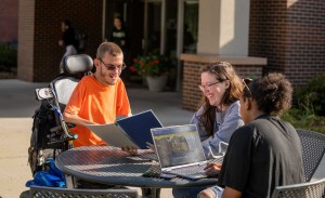 A group of students sit at an outdoor table talking and studying.