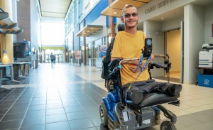 A college student sits in his wheelchair and smiles for a photo.