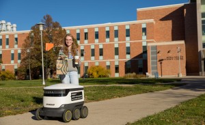 A woman hold her lunch that was delivered by a small, white robot.