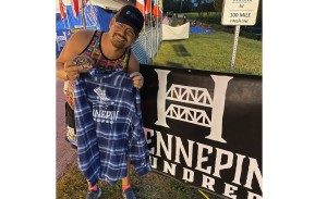 A man poses with a shirt and belt buckle he received for completing a 100-mile race.