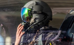 A fighter pilot sits in a cockpit wearing a helmet.