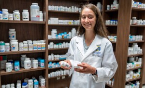 A pharmacy student in a white lab coat holds two pill bottles.