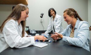 A pharmacy student practices a procedure while a professor looks on.