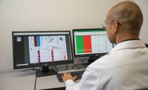 A man looks at two computer screens with green and red columns.