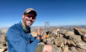 A man sitting on a mountain gives the thumbs up while conducting a science experiment using Diet Coke.