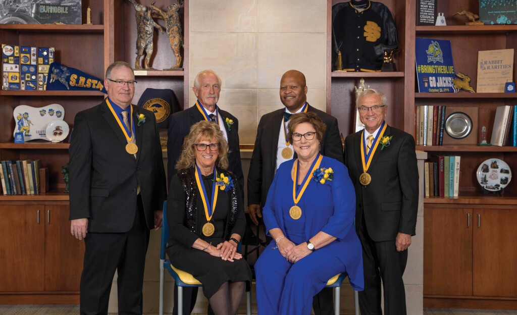 Six adults pose for a photo wearing distinguished alumni medals.