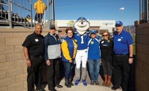Six distinguished alumni pose with Jack the Jackrabbit on the edge of the football field.