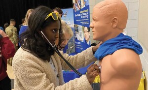 A middle school student uses a stethoscope on a mannequin.  