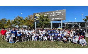 A large group of middle school students pose for a photo outside a football stadium.