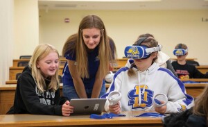 A middle school student tries a virtual reality headset while two other students watch.