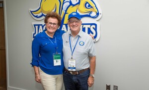 A couple smile for a photo in front of a large jackrabbit logo on the wall.