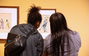 The backs of two people as they look at a native american painting.