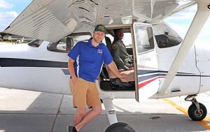 A student sits in an airplane with a flight instructor standing in the door to the plane.