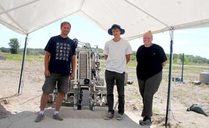 A professor stands with two students under a white canopy with the machine they built for a NASA contest.