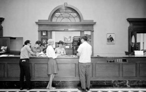 A black and white photo shows students standing at the original circulation desk.