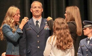 A man in a military uniform stands at attention while his wife and daughters place pins on his uniform.